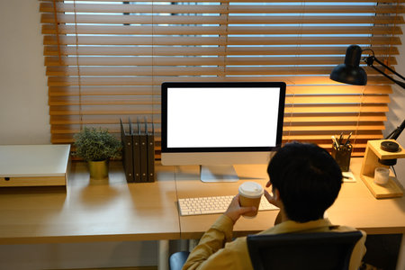 Creative man working on computer with blank screen and holding coffee cup.