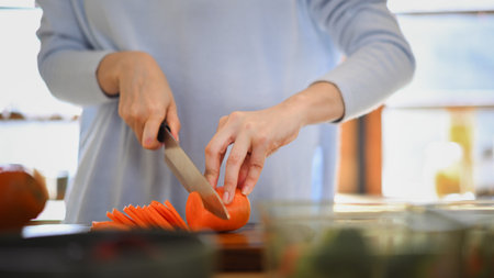 Closeup of young female hands chopping fresh orange carrot on board while in modern kitchen.の写真素材