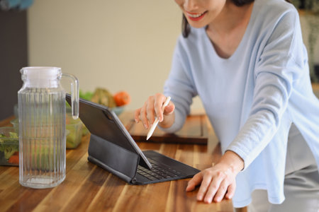 Cropped shot smiling woman using tablet to follow online recipe while preparing healthy food in cozy kitchen, showing lifestyle balance.の写真素材