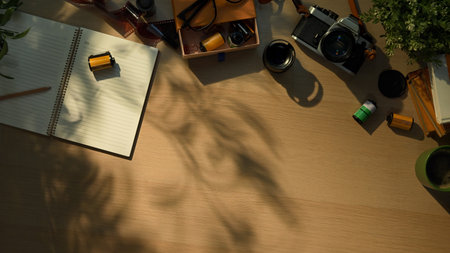 Creative workspace with vintage camera, notebook, and coffee cup in warm morning sunlight.の写真素材