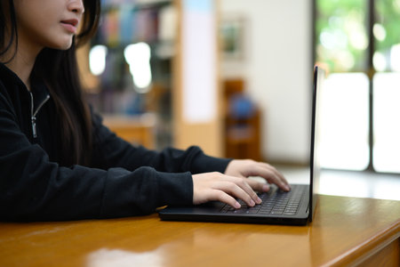 Cropped shot teenage asian woman education or internet encyclopedia concept. Open laptop in library.の写真素材