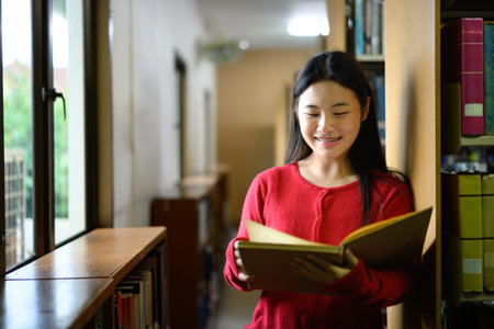 An Asian girl is reading a book in a library.の写真素材