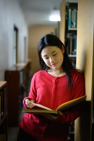 An Asian girl is reading a book in a library.