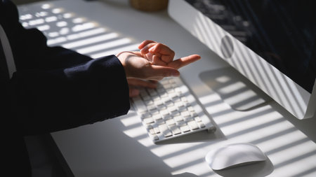 A hand pointing toward the screen above a keyboard with calm light and shadow on the desk.の写真素材