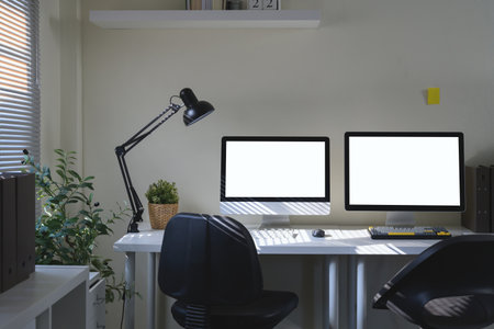 A workspace featuring a two computer monitor, desk lamp, and office supply elements.