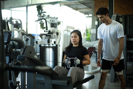 Trainer supervising woman during seated row workout.