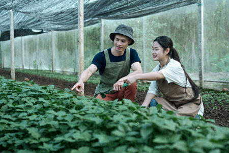 An experienced grower teaching a young girl farmer inside a shaded greenhouse.