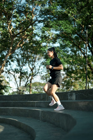 Female runner jogging down concrete steps during outdoor workout in urban park with morning light.