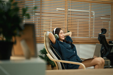 Smiling woman wearing headphones listen to music playing in laptop computer.の写真素材