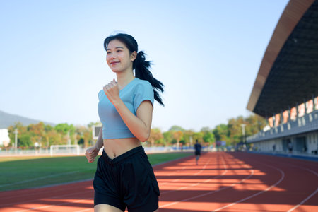 Young Asian woman jogging on outdoor running track in morning sunlight.の写真素材