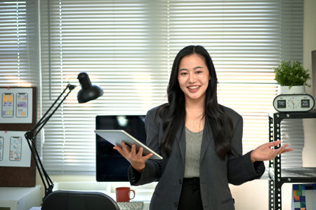 Confident businesswoman presenting ideas with tablet in modern office, professional leadership concept.の写真素材