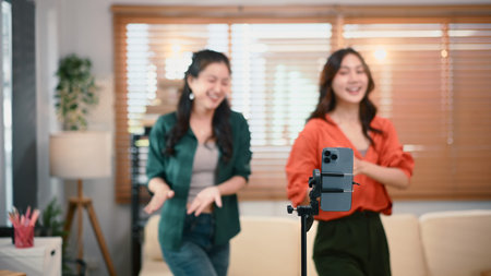 Two girl dancing and making videos filming vlog with online content focus with smartphone.