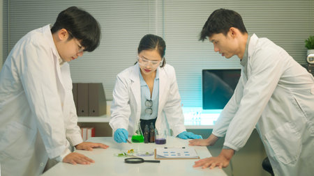 Three science collaborate around a lab table, analyzing plant samples and chemical solutions together.の写真素材