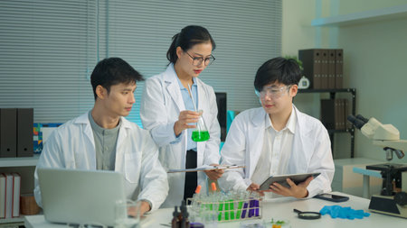Research team discusses results while a scientist presents a green liquid sample, showing collaboration and analysis in a modern laboratory..の写真素材