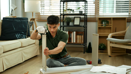 Man assembling flat pack furniture at home, using tools with focus and precision in a modern living room.の写真素材