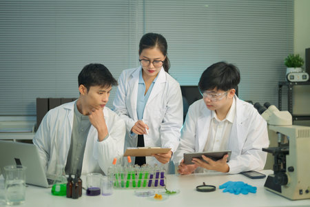 Research team in lab coats analyzing test samples and recording data with laptop and tablet in a...