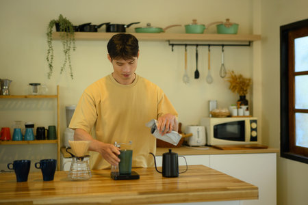 A young man prepares pour-over coffee in a cozy home kitchen, measuring beans and enjoying a calm morning routine.の写真素材