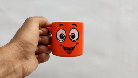 Human hand holding an orange smiley coffee mugの写真素材