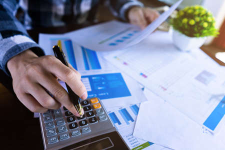 Close up businessman using calculator and reading paper document about business data, accountancy...
