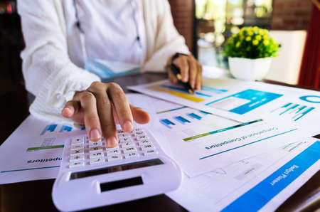 Close up businesswoman hand using a calculator and pointing graph report document about cost, tax,...