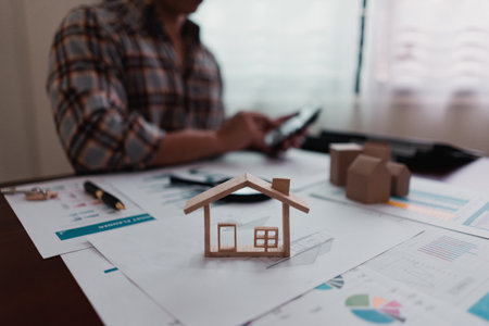 Real estate agents are calculating the house price on the table with the house model, the house purchase contract, the house design documents, the keys.の写真素材
