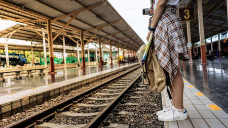 Young girl Traveler tourist woman carrying backpack, camera, travel map, hat walking and waits for train on railway platform.の写真素材