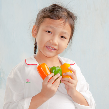 little girl holding capsicum in kitchenの写真素材