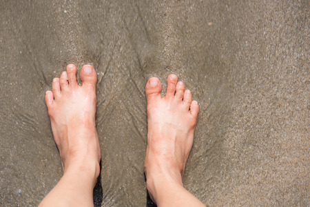 Bare female feet on the shore washed by the seaの写真素材