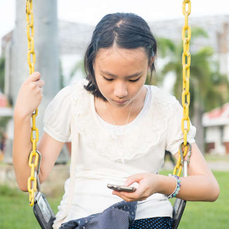 Asian teen playing smartphone in playgroundの写真素材