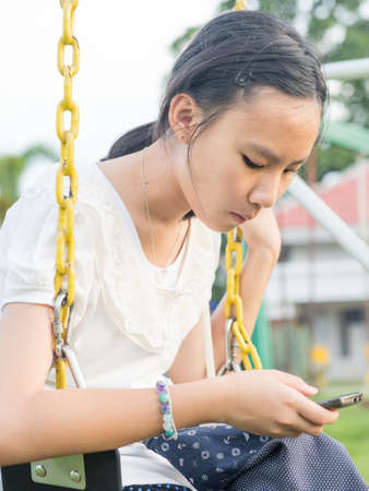 Asian teen playing smartphone in playgroundの写真素材
