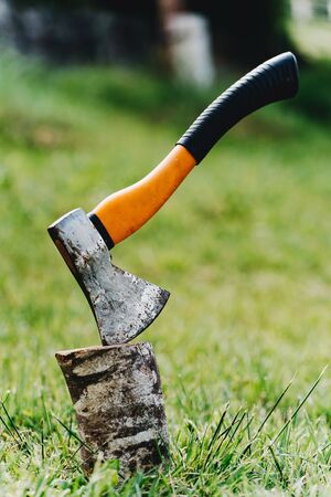 Axe with orange handle sticks out in hemp against the background of green grass