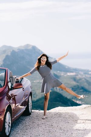 Happy woman stay near red convertible car with a beautiful viewの写真素材