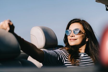 Happy woman sits in a red convertible car with a beautiful view