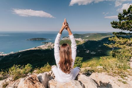 Girl in lotus pose on top of mountain in white clothes