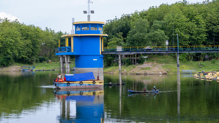 Brebes, Indonesia - Dec 12, 2021: Water level control tower in Malahayu Reservoir with forest background and fishing boats around it.のeditorial素材
