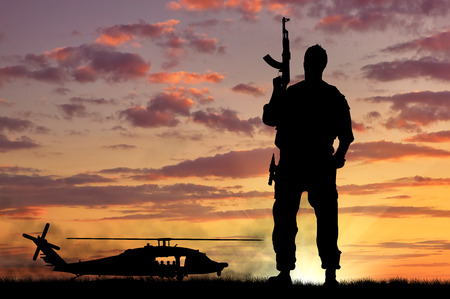 Silhouette of a soldier and helicopter at sunsetの写真素材