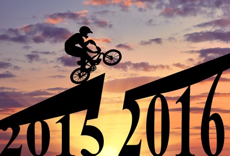 Concept of the new year. Extreme cyclist makes a jump between 2015 and 2016 years at sunsetの写真素材
