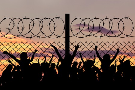 Concept of security. Silhouette of refugees climb over the barbed wire at the borderの写真素材