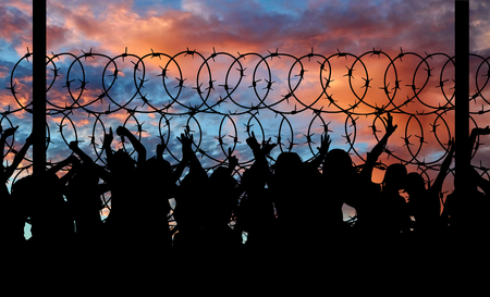 Concept of security. Silhouette of refugees climb over the barbed wire at the borderの写真素材