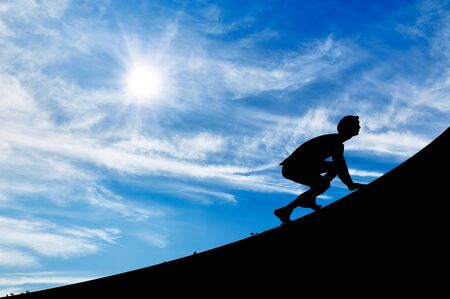 Silhouette of a man scrambling up on the background of the sunny skyの写真素材