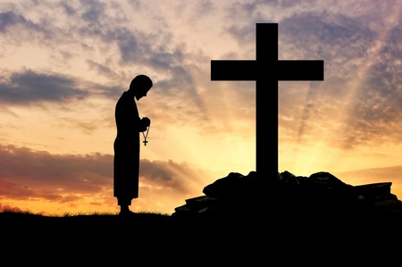Concept of religion. Silhouette of priest and cross on a background of beautiful skyの写真素材