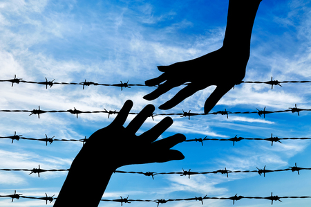 Concept of refugee. Silhouette helping hand to refugees on the background of the fence of barbed wireの写真素材