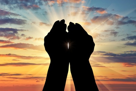 ?oncept of Islam, the Koran. Silhouette of praying hands facing the sky at sunsetの写真素材