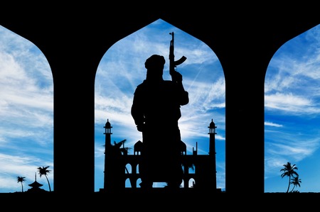 Concept of terrorism. Silhouette of a terrorist with a weapon on the background of the town hallの写真素材