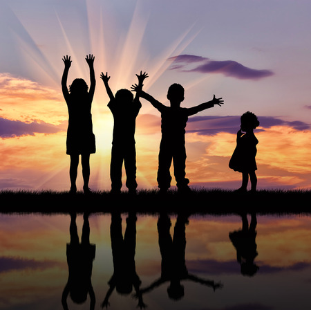 Concept of happiness. Silhouette of happy children on a background of beautiful sky and reflection in waterの写真素材