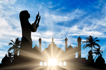 Concept of the Islamic religion. Silhouette of praying woman against the backdrop of the town hall at dawnの写真素材