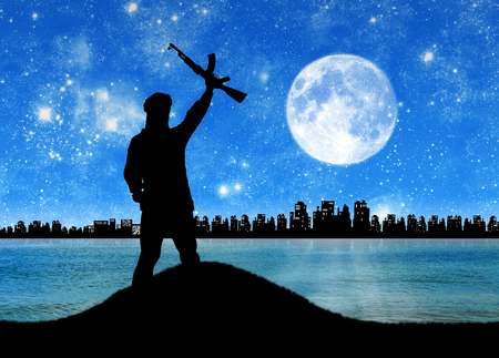 Concept of a terrorist. Silhouette of a terrorist in front of a night city and moonの写真素材