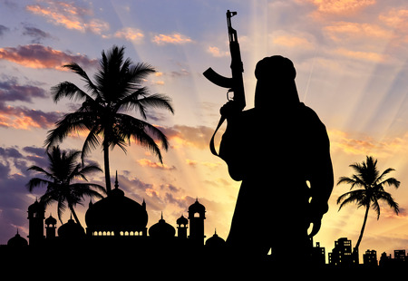 Concept of terrorism. Silhouette of a terrorist with weapons near the town hall at sunsetの写真素材
