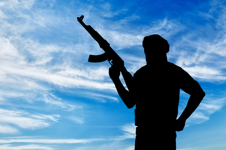 Concept of terrorism. Silhouette of a terrorist with a weapon against a blue skyの写真素材