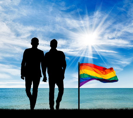 Concept of gay people. Silhouette of two gay men on a walk by the sea during the day and a rainbow flagの写真素材